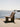 A woven outdoor lounge chair with a ribbed backrest sits on a concrete pier with a body of water and a wooden dock in the background.