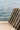 A close-up of a ribbed, textured outdoor lounge chair cushion in a warm taupe-brown color, positioned against a blurred background of shimmering blue water.