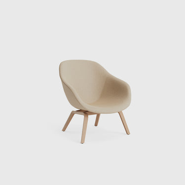 A minimalist beige upholstered lounge chair with an angular backrest and wooden frame.