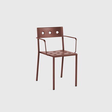 A modern metal armchair with a slatted backrest featuring three circular cutouts, armrests, and a perforated seat, shown in a warm reddish-brown finish against a light gray background.