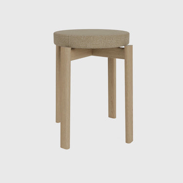 A modern round stool with a textured beige fabric cushioned seat and light oak wood legs, shown against a solid light gray background.