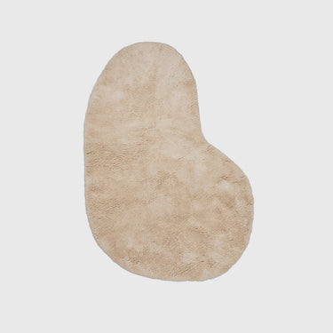 A beige, plush, shaggy area rug with an organic, asymmetrical shape, shown flat against a light gray background.