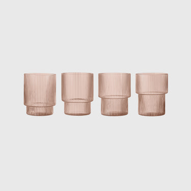 Four ribbed glass tumblers in a translucent dusty rose color, arranged in a row against a light gray background.