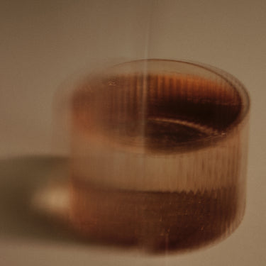 A close-up of a translucent amber-brown cylindrical container or cup with a ribbed texture, photographed in warm dim lighting against a beige background.