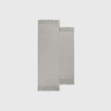 A natural wool rug with a geometric pattern, featuring long panels and tassels on the sides.