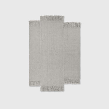 A natural wool rug with a geometric pattern, featuring long panels and tassels on the sides.