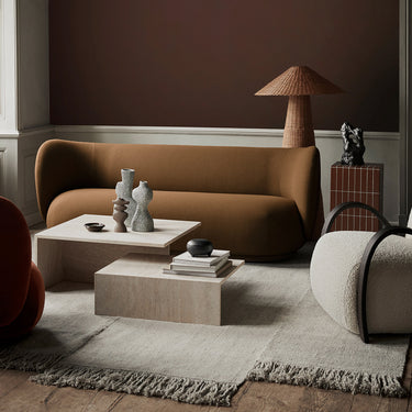 A natural wool rug with a geometric pattern, featuring long panels and tassels on the sides. In an interior space with a brown sofa, coffee table and floor lamp.