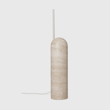 A modern cylindrical table lamp with a rounded top, crafted from beige travertine stone, featuring a slim white cord and a thin vertical white stem, set against a solid light gray background.