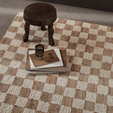 Interior image of checkered jute rug in a living space with a dark wooden stool.