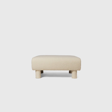 A beige upholstered ottoman with a simple, contemporary design, featuring a flat rectangular cushion for seating.