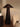 A dark brown woven floor lamp with a tapered conical shade and textured base, styled in a warm, neutral-toned room next to a textured armchair and a side table.