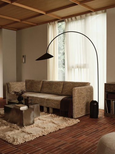 A modern living room featuring a textured beige fabric sofa, a tall black arched floor lamp, a shag rug, and a wood ceiling.