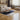 A modern living room setting featuring a beige Kelim rug with geometric shapes and a cozy seating area consisting of a sofa, loveseat, and two ottomans on a wooden floor.