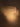 A close-up of a ribbed, translucent frosted light box or lamp emitting a warm golden glow against a dark brown background.