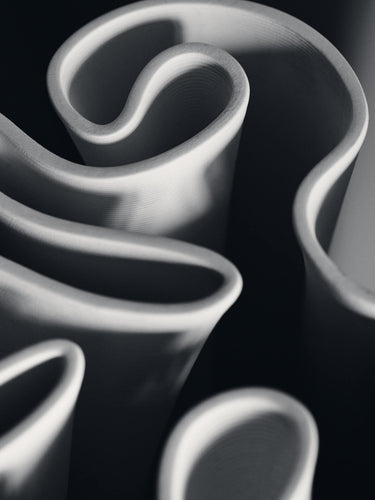 Abstract close-up of sculptural rolled and curved white forms against a dark black background.