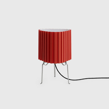 A modern red pleated table lamp with slim silver metal legs and a black power cord, shown against a light gray background.
