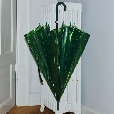 Green umbrella leaning against a white radiator in a room.