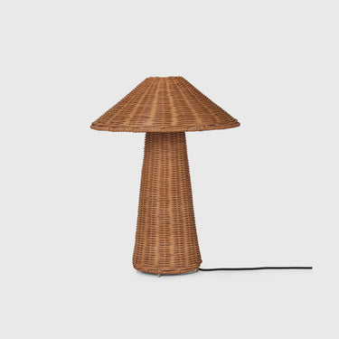 A mushroom-shaped table lamp made of woven natural wicker, featuring a wide conical cap and a textured cylindrical stem, with a black power cord extending to the right, set against a solid light gray background.