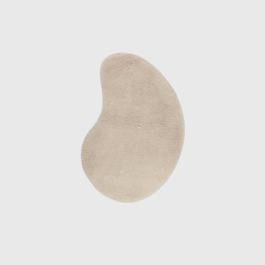 An organic-shaped beige plush rug centered on a light gray background.