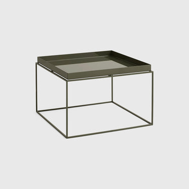 A minimalist square side table featuring a light olive green tray on top of a thin, open-frame metal base in a matching olive tone, set against a solid light grey background.