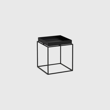 A modern black side table featuring a square tray top and an open cube wireframe base, shown against a solid light gray background.