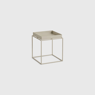 A modern square side table featuring a light beige tray top and a minimalist open cube metal frame base, shown on a solid light gray background.
