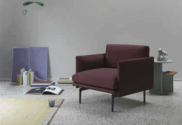 A modern armchair upholstered in deep burgundy fabric with slim black metal legs, set in a minimalist room with a gray wall, terrazzo floor, and styled decor.