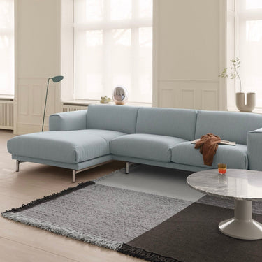 A light blue sectional sofa with a chaise lounge in a bright, modern living room with cream walls, a gray and black rug, and a marble-top side table.