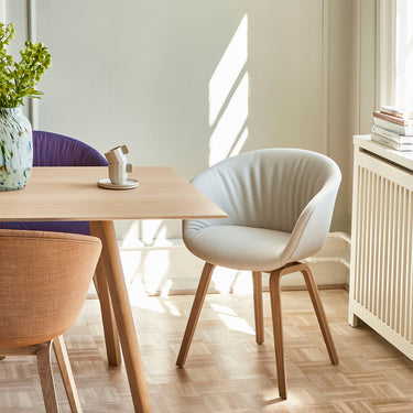 A modern white upholstered AAC 23 Soft chair with a wooden frame, pictured in an interior setting with a table and radiator in the background.