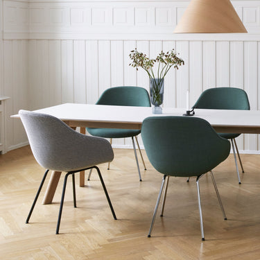 A set of modern dining chairs with upholstered seats and four-legged steel frames, arranged around a table in a room with wooden flooring and white walls.