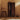Wooden cabinet with open door, stool, and shoes on a patterned rug against a beige wall.