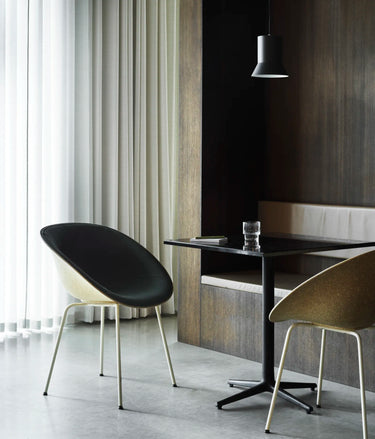 Modern dining room corner with two upholstered chairs and a black table, set in a real interior with curtains, wood paneling, and a pendant light.