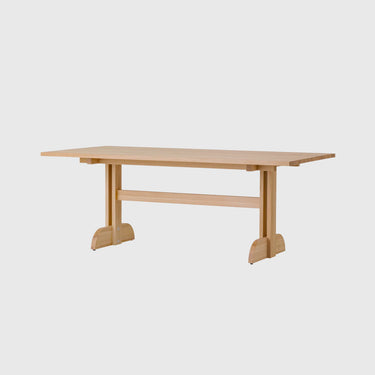 A light natural wood dining table with a rectangular top, apron base, and decorative feet, shown against a plain light grey background.
