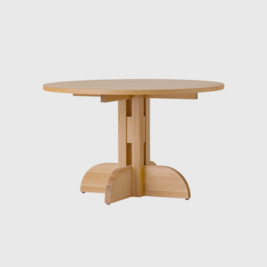 A light natural wood pedestal dining table with a round top and a unique split base, shown against a solid light gray background.