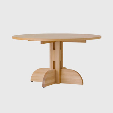 A light natural wood round dining table with a unique pedestal base featuring three curved support legs, shown against a solid light grey background.