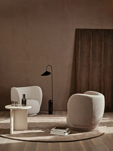 Modern interior with two beige armchairs, a small table, and a floor lamp against a brown wall.