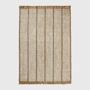 A rectangular woven rug with a natural jute texture, featuring vertical tan stripes and fringed edges on a light gray background.