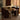 A modern dining set featuring a rectangular glass-top table with brushed metal legs and four dark brown upholstered chairs, styled in a warm, sunlit room.