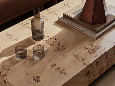Interior image of a table top of a burl coffee table with a glass carafe and glasses.