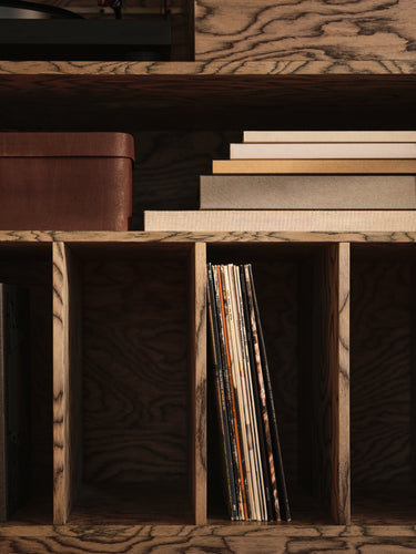 Close-up of a rustic wooden shelving unit with cubby dividers, holding stacked books, a brown box, and a vertical row of vinyl records.
