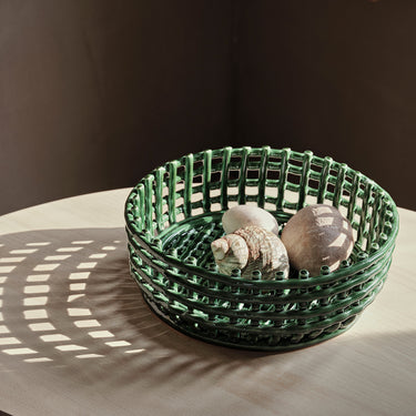 A handmade ceramic centrepiece in emerald green color, displayed on a table with some spherical objects inside it, possibly a fruit or bread basket.