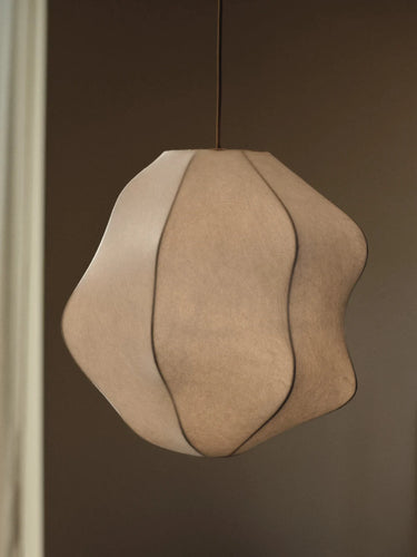 An organic-shaped pendant light with a textured beige fabric shade, suspended by a thin black cord against a dark brown background.