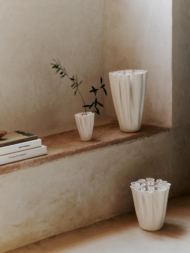 Three white ceramic vases on a wooden shelf against a beige wall.