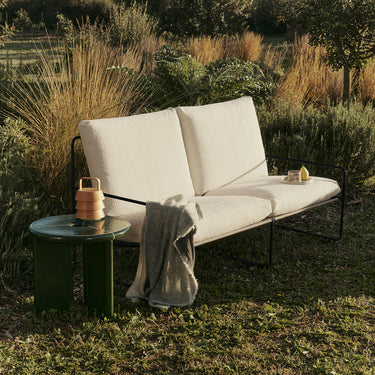 Exterior image of a 2 seater outdoor sofa in boucle surrounded by a garden.