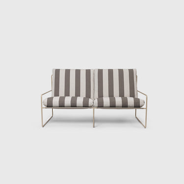 A two-seater outdoor sofa with striped black and chocolate cushions, featuring a steel frame, placed on a outdoor setting with plants in the background.
