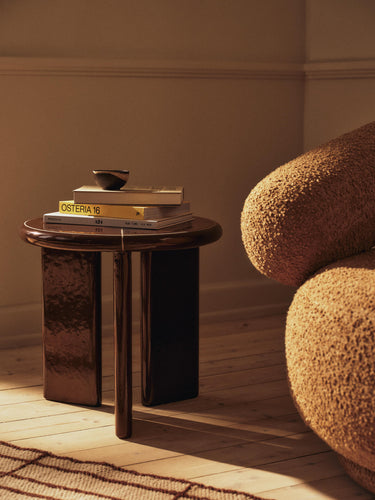 Small round table with books next to a textured armchair in a room with wooden flooring.