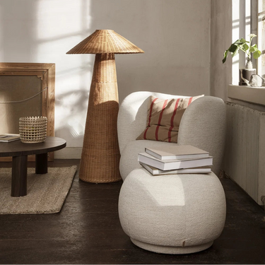 Modern living room with a wicker floor lamp, white armchair, and round ottoman.