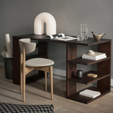 Interior image of a dark stained wood desk in a home office setting with a chair, table lamp and various desk decorative items. 