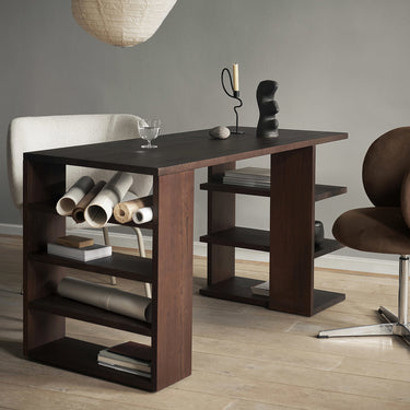An interior image of a viewpoint of a dark stained wood desk in a home office with two chairs, a rice paper light shape pendant and various desk top objects.