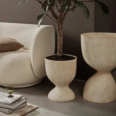 Interior image of two freestanding stone plant pots with an indoor tree planted with a cream sofa.